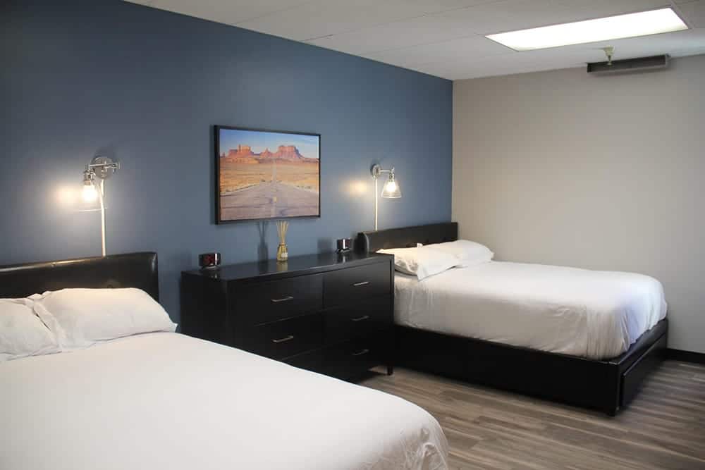 Room with two double beds and a dresser under artwork