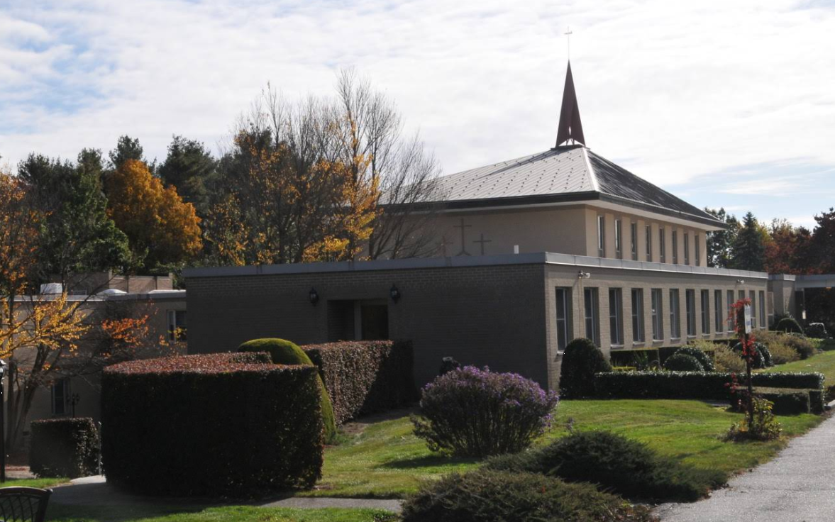 Brick chapel with tall steeple surrounded by trimmed bushes and trees