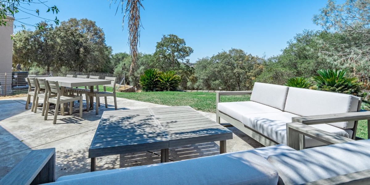 Patio with cushioned seating and a dining table overlooking greenery.