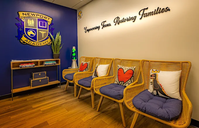 Waiting area with wicker chairs, colorful pillows, and academy crest on the wall