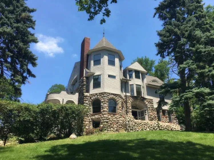 Historic stone residence surrounded by trees and landscaped lawn