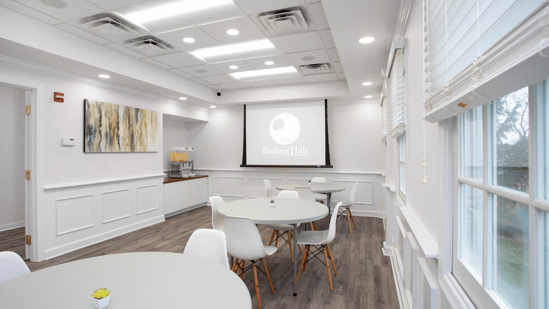 Dining area with  tables and chairs in front of a projector screen.