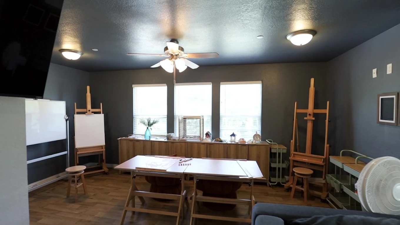 Recreational art room with easels, worktables, storage cabinets, large windows, and ceiling fans