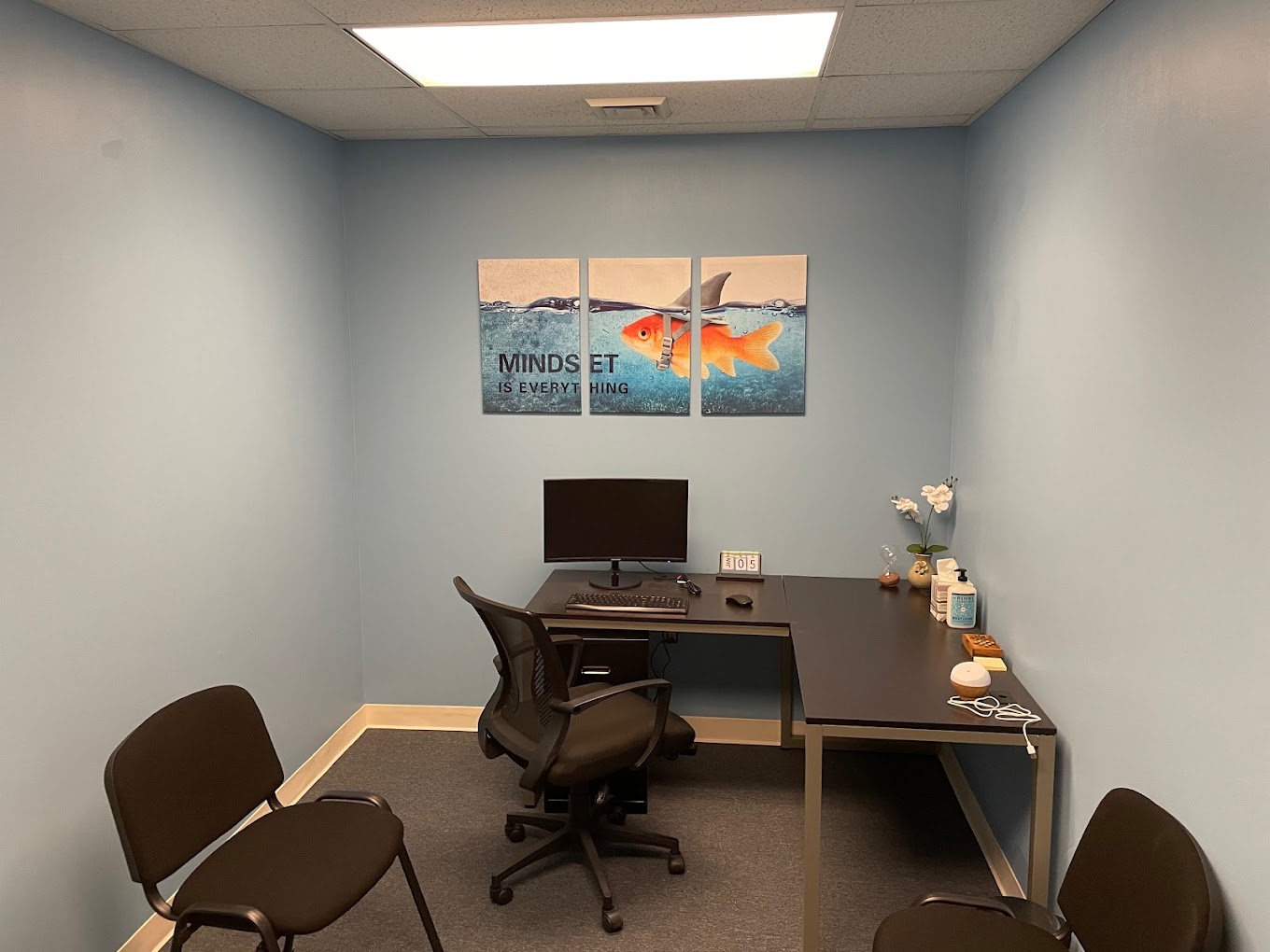 Therapy room with a computer desk, chairs, and artwork.