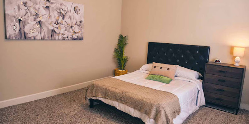 A serene bedroom with a plush bed featuring a tufted headboard, soft linens, a bedside table with a lamp, and calming floral artwork.