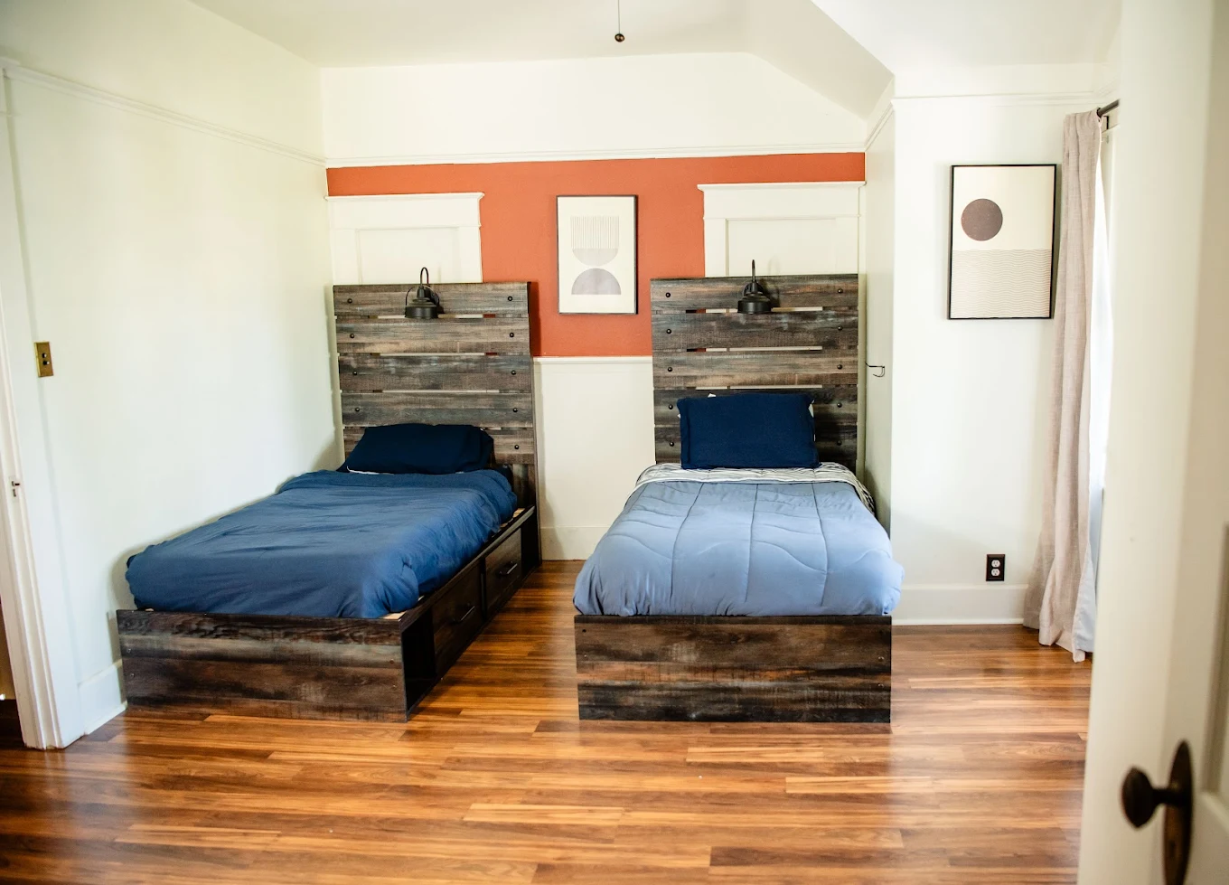 Two twin beds with wooden headboards in a warmly decorated recovery residence bedroom