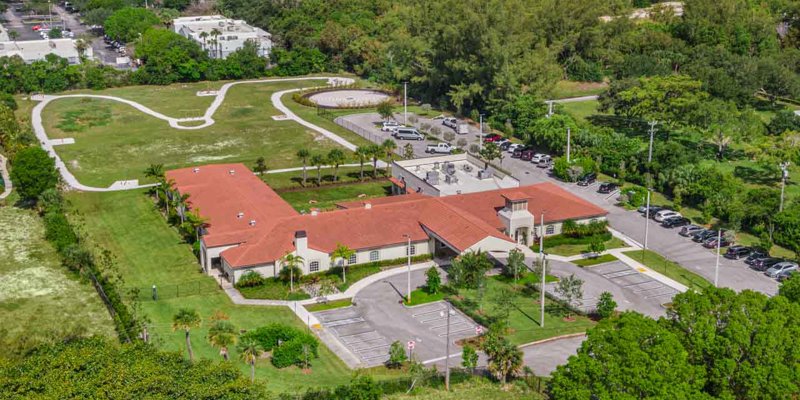 An aerial view of a large facility with red roofs, surrounded by greenery, walking paths, and ample parking. A peaceful and spacious environment.