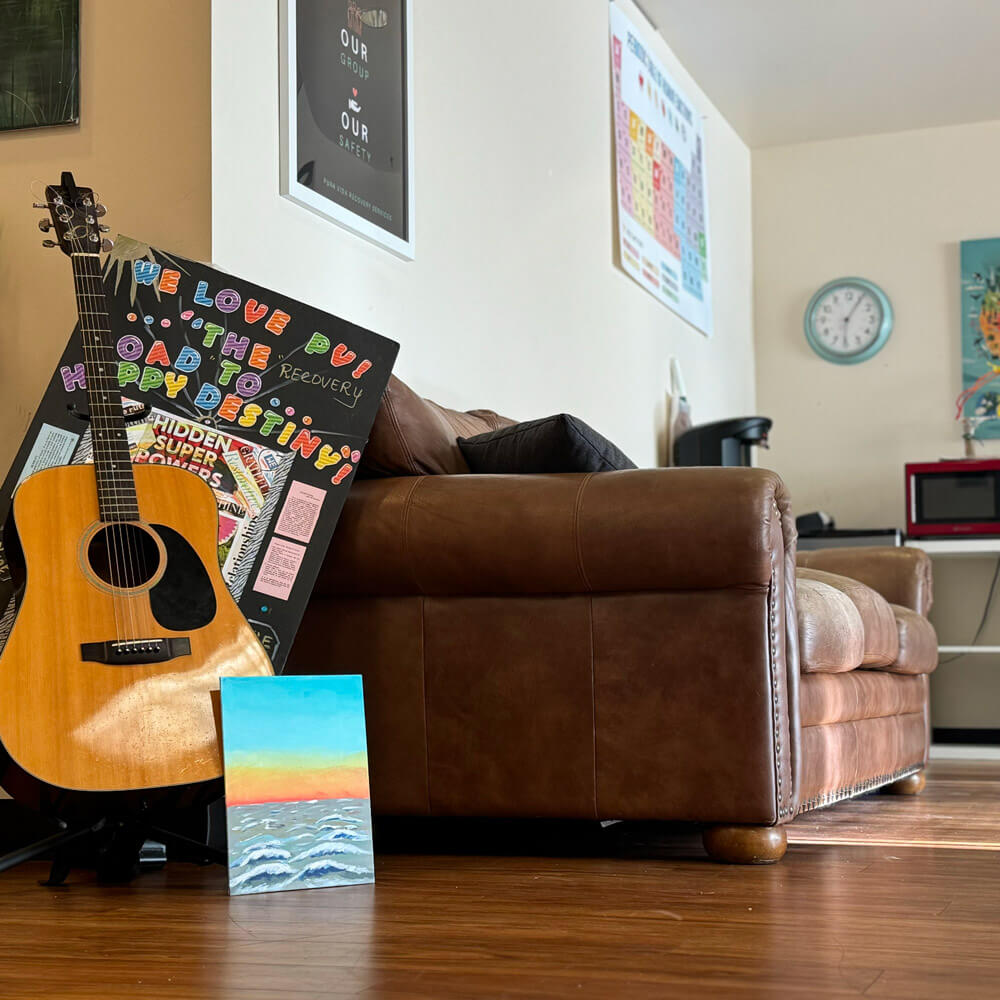 Guitar, art board, and painting next to brown leather couch