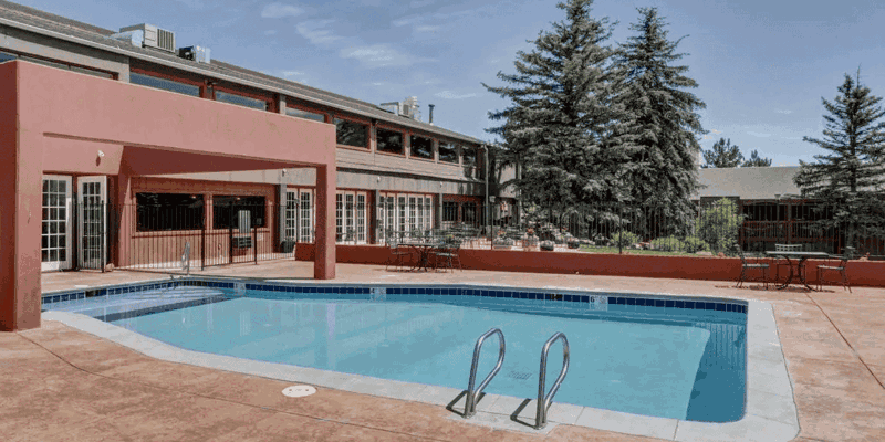 Inviting outdoor pool area with surrounding patio, lounge seating, and lush greenery, perfect for relaxation in a serene environment.