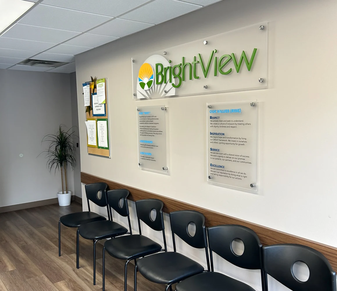 BrightView Health waiting area with black chairs, wall-mounted BrightView logo and informational displays, wood-look flooring, and a potted plant