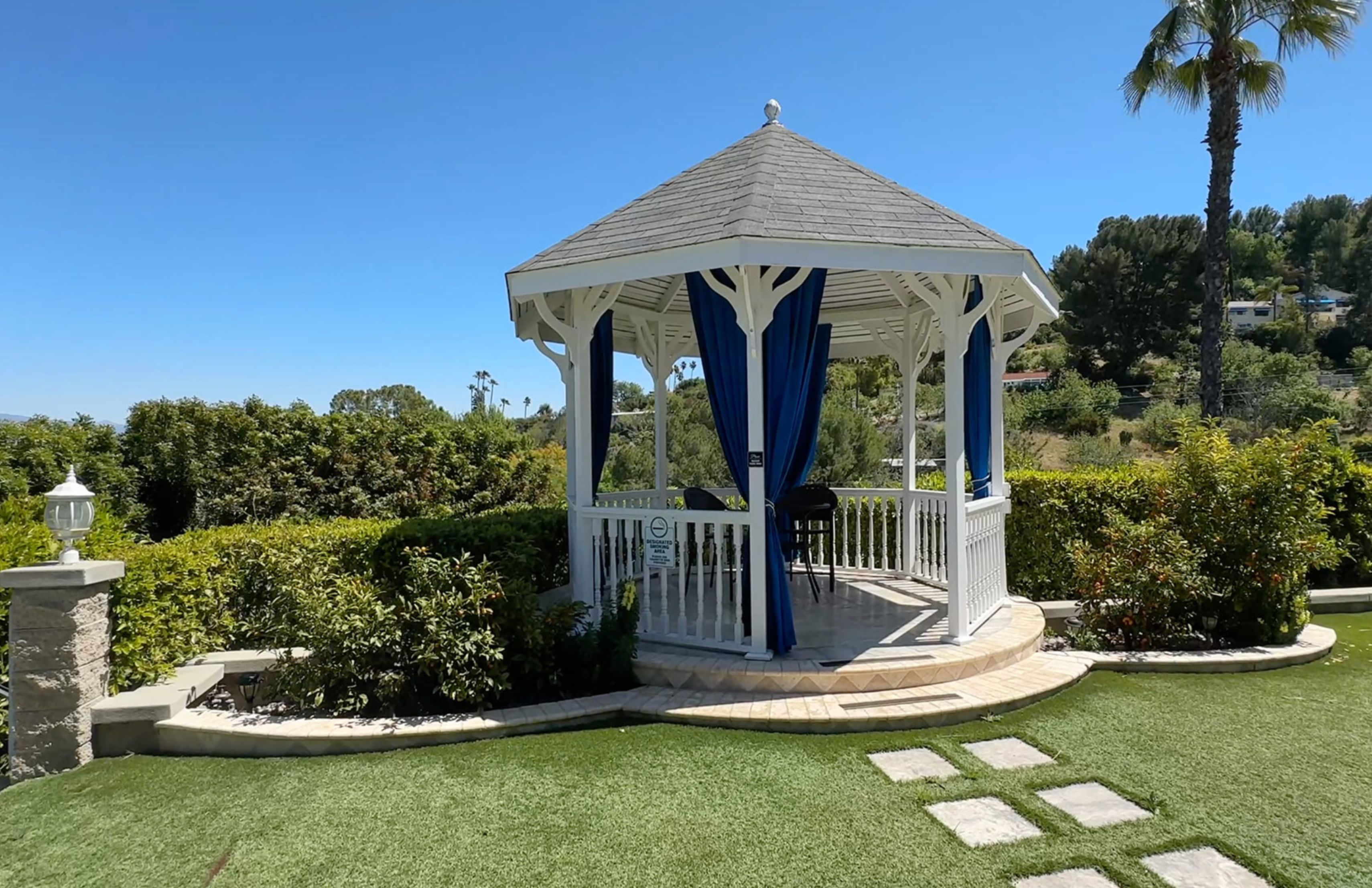 A white gazebo with blue curtains overlooking green hills.