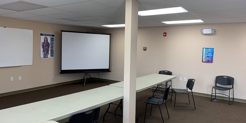 A bright and clean meeting room with ample seating and a projector screen, providing a comfortable space for group discussions or presentations.