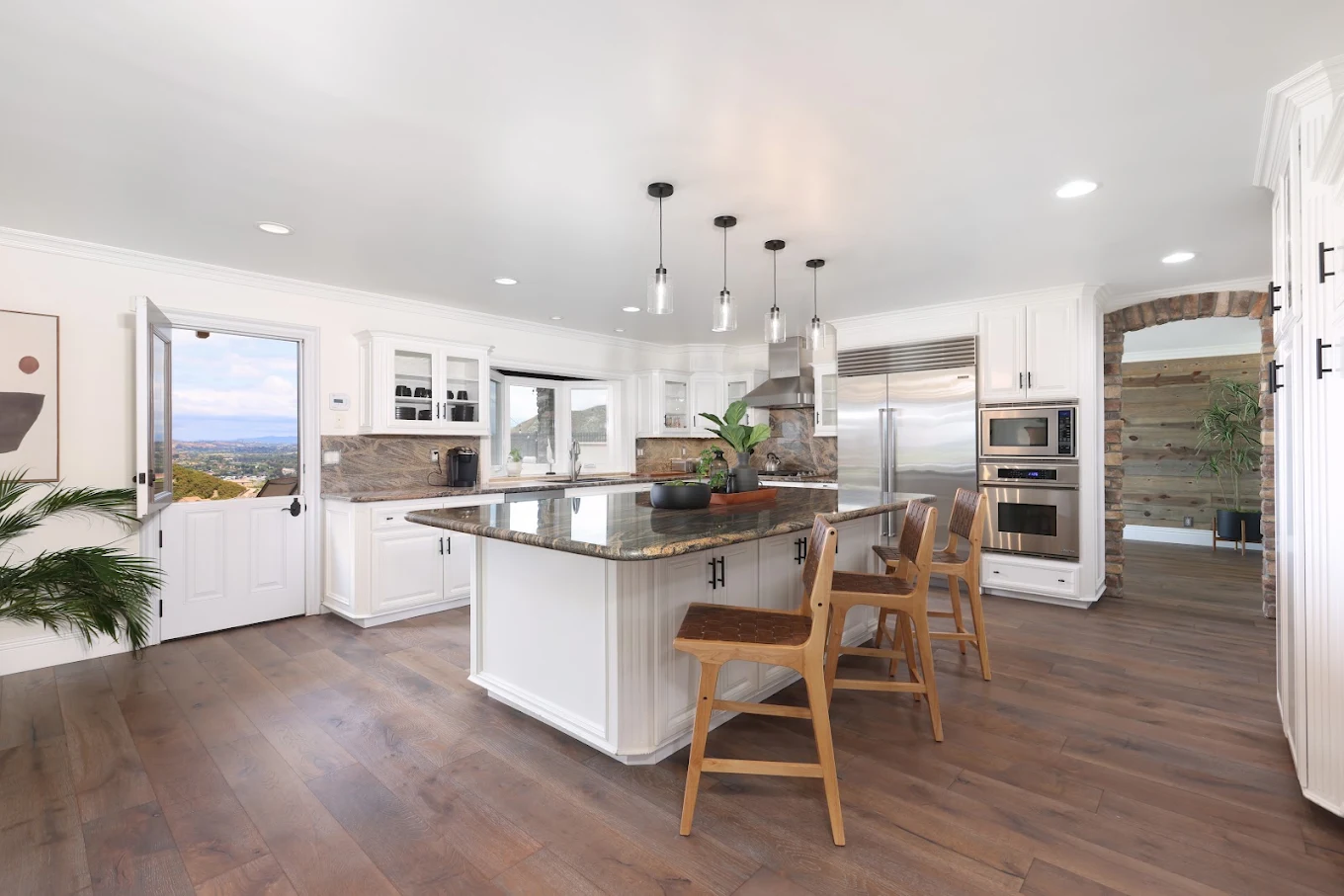 Bright kitchen with large island, stools, and hillside view