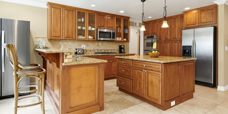 A spacious kitchen with warm wood cabinets, granite countertops, a center island, stainless steel appliances, and bar stools, creating an inviting space.