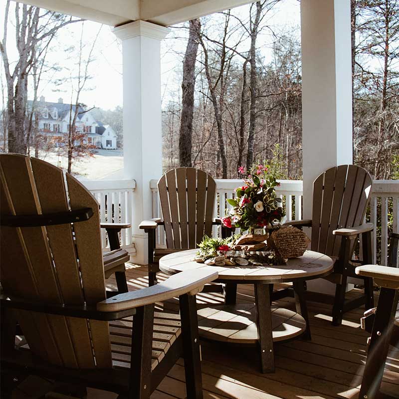 Covered porch with Adirondack chairs and table overlooking wooded area