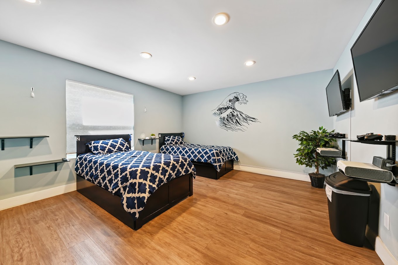 Bedroom with matching twin beds, wave wall art, and gaming shelves.