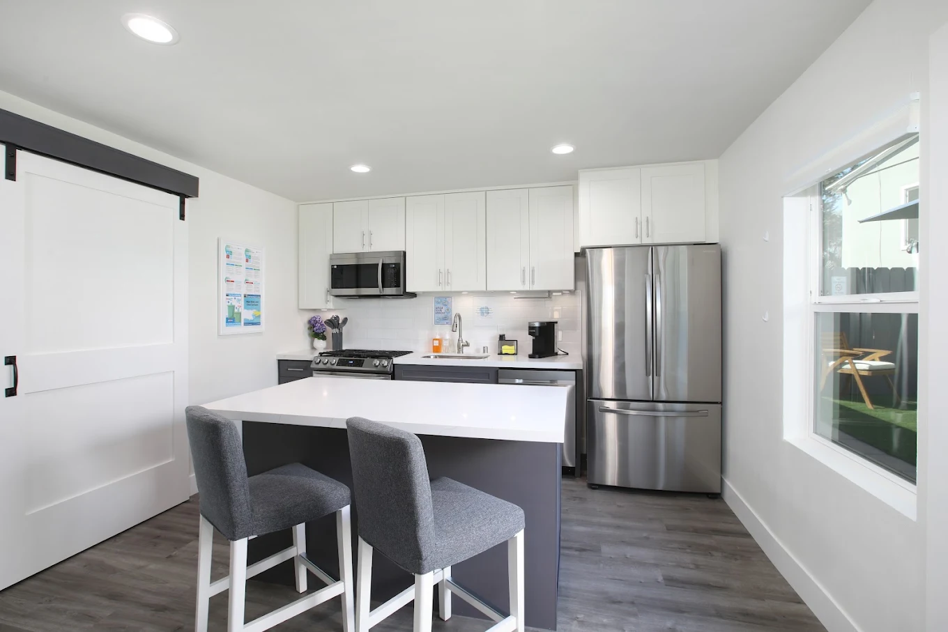 Modern kitchen with white cabinetry, stainless steel appliances, large island, and gray upholstered stools