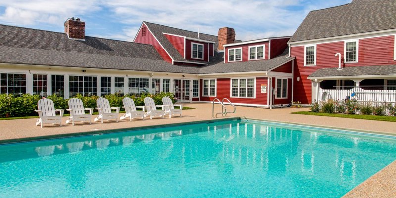 A refreshing outdoor pool area with Adirondack chairs lined up beside a charming red building, offering a perfect spot for relaxation and leisure.