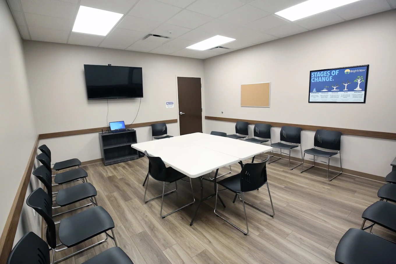 BrightView Elyria group room with tables, chairs, television, and Stages of Change poster