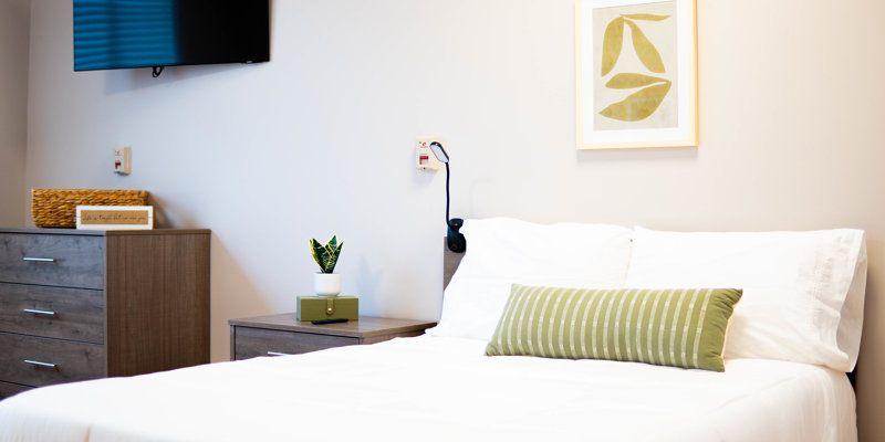 Bright and inviting bedroom featuring a neatly made bed with soft linens, modern wooden furniture, stylish decor, and a wall-mounted TV.