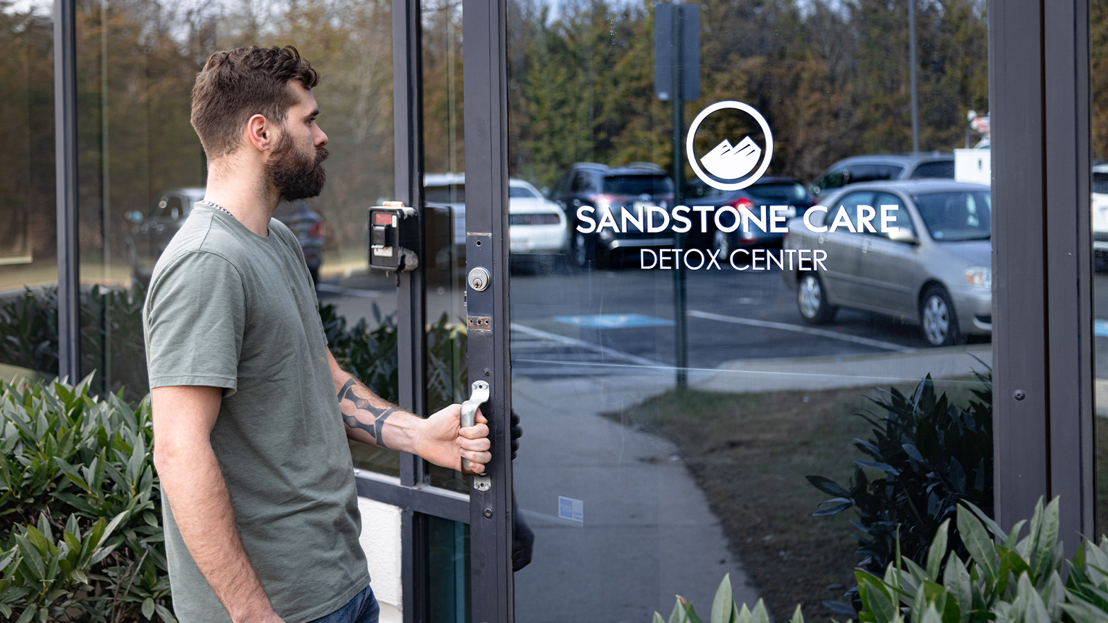 Man opening the glass door of a Sandstone Care detox center.