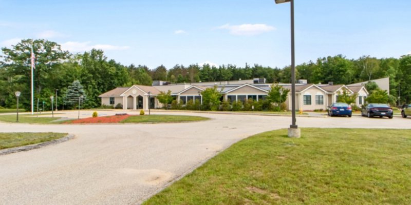 A large, single-story building with a circular driveway, surrounded by greenery and trees, offering a peaceful and welcoming atmosphere with ample parking.