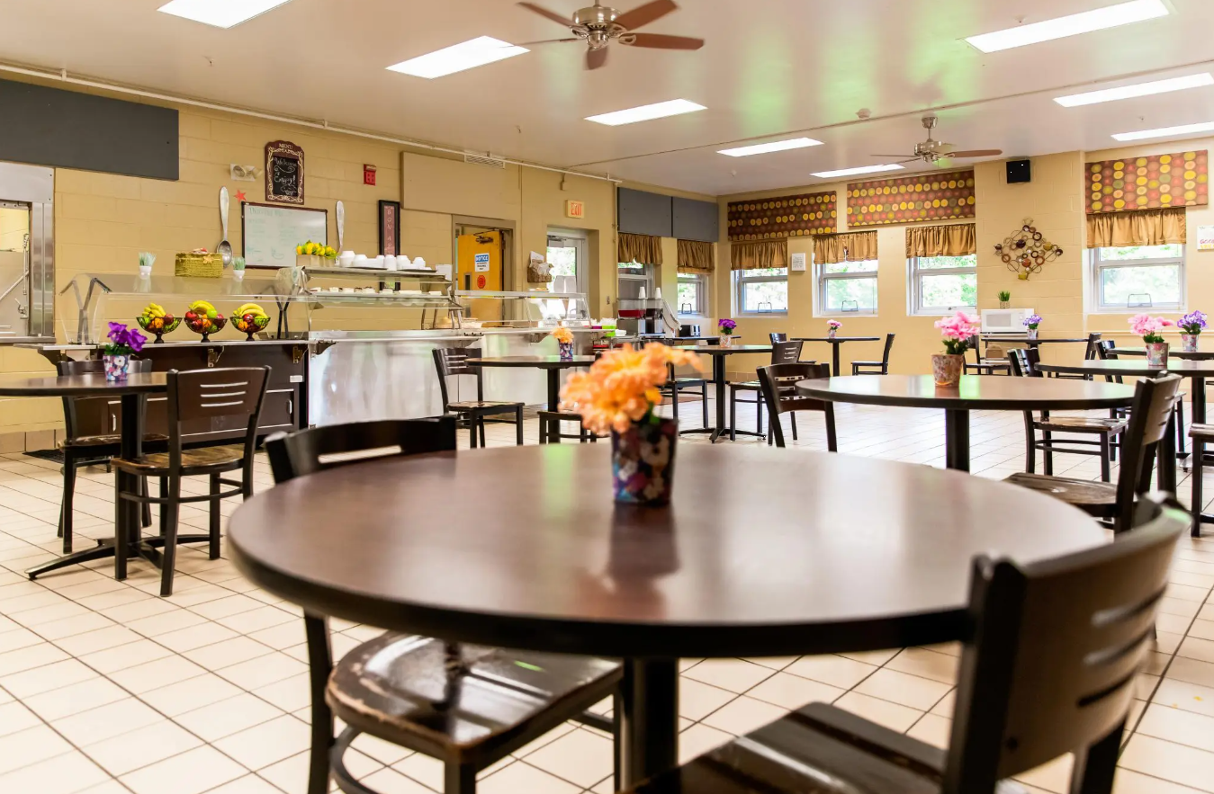 Bright dining hall with tables, chairs, and a food service counter