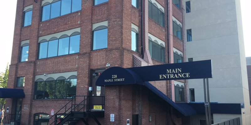 A brick building with large windows and a blue awning over the main entrance, providing a welcoming and professional exterior.