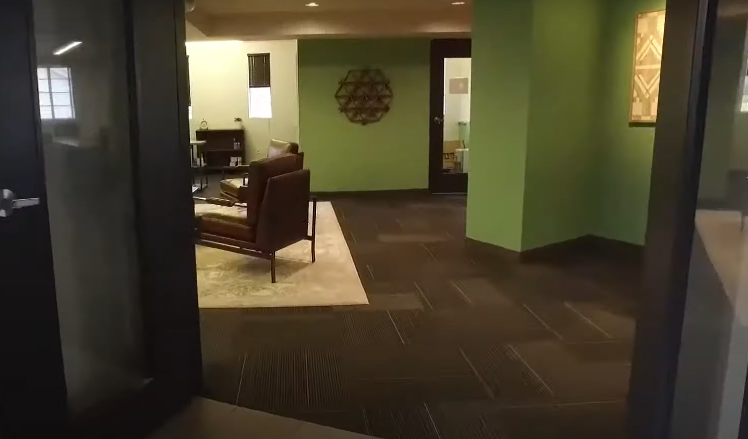 A hallway with green walls leading to a seating area with leather chairs