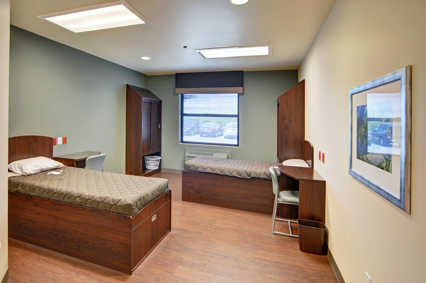 A clean, shared bedroom with two twin beds, built-in wardrobes, desks, and a window providing natural light