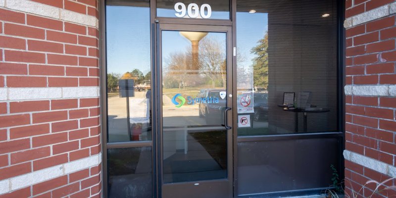  The entrance to a brick building with glass doors displaying the "Symetria" logo, providing a professional and welcoming entry point for visitors.