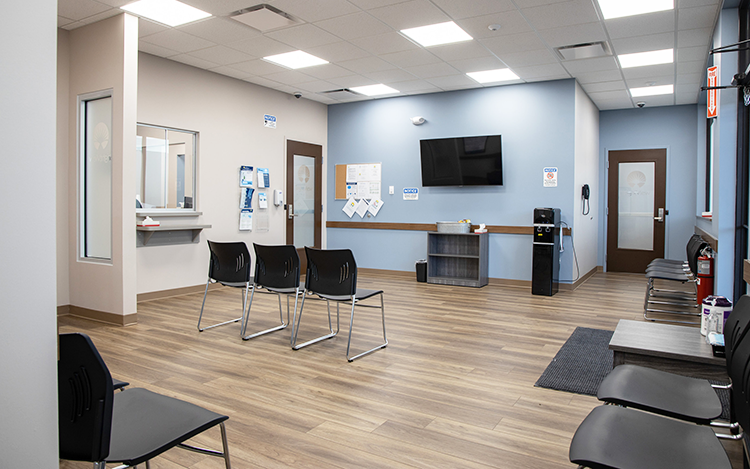 Bright lobby with reception window, chairs, and wall-mounted TV