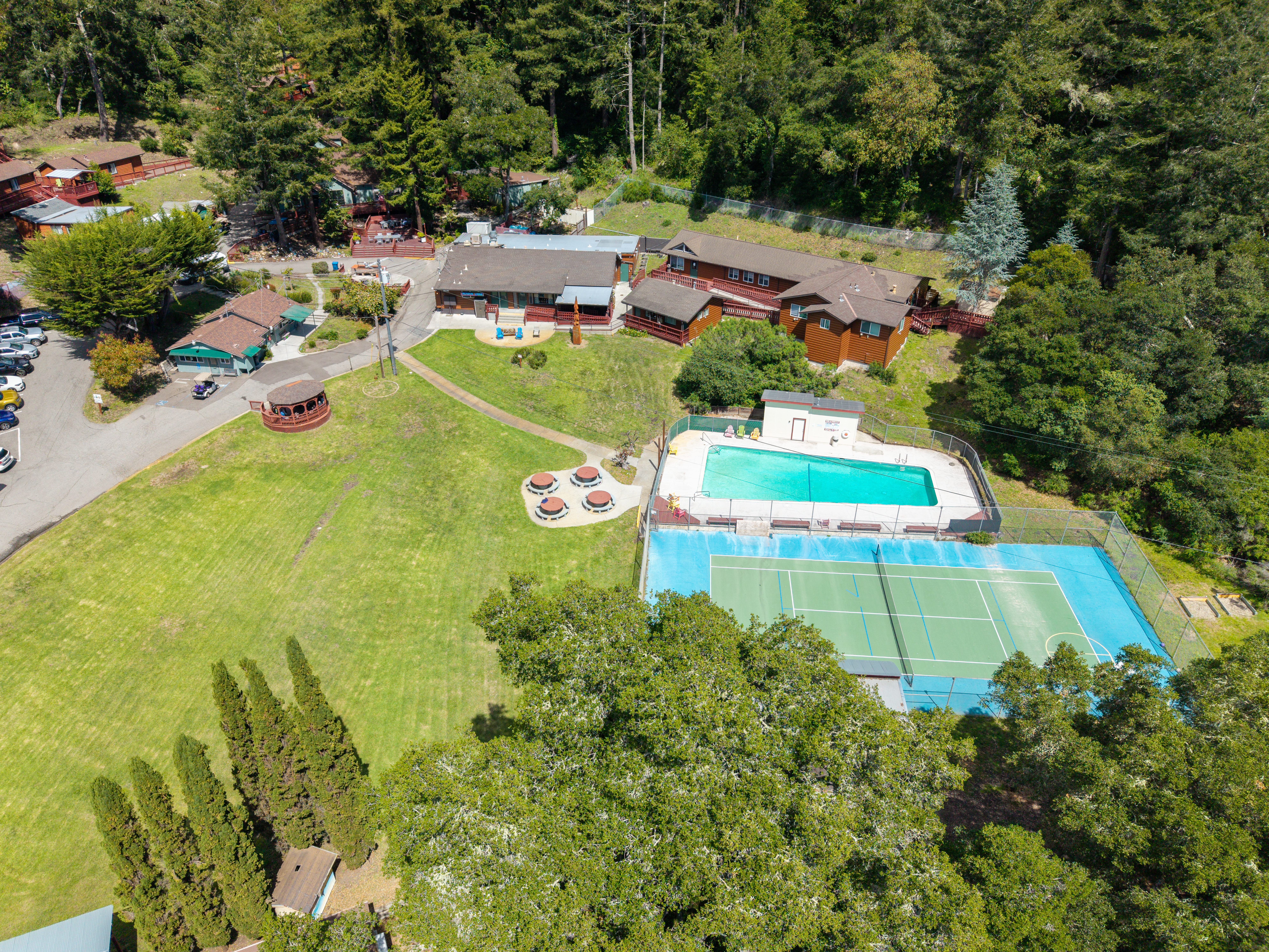 Aerial view of campus with pool, sports court, and wooded grounds