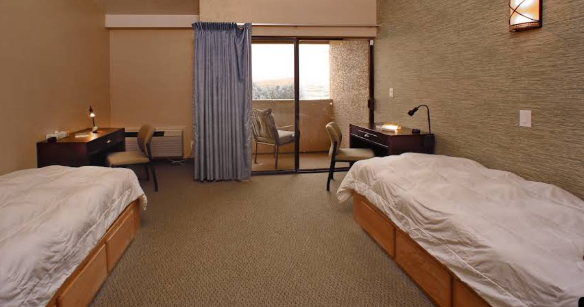 Two-bed room with desks and sliding door to balcony