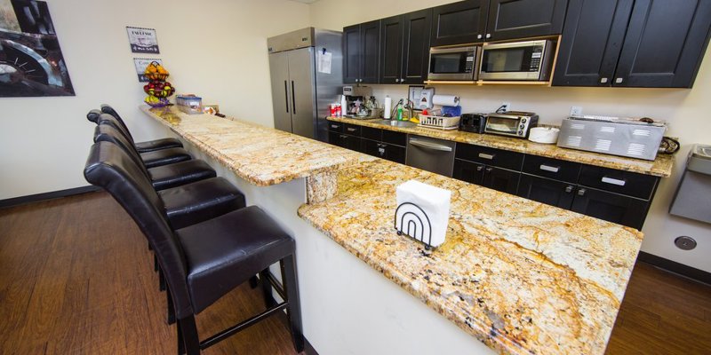 A modern kitchen area with a long granite countertop, sleek black cabinets, and comfortable barstools, offering a stylish and functional space for dining.