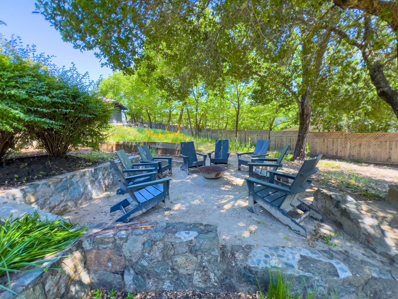 Outdoor chairs arranged around a fire pit under trees