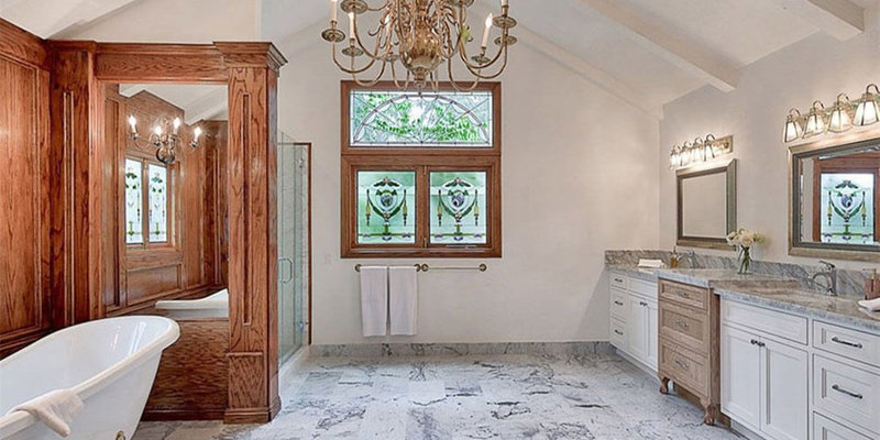 A luxurious bathroom with elegant marble floors, a chandelier, stained glass windows, a clawfoot tub, and double vanities, blending classic and modern styles.