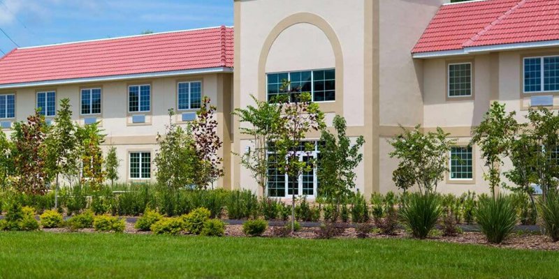  A bright, modern facility with a red-tiled roof and lush landscaping featuring neatly trimmed greenery and trees, creating a welcoming atmosphere.