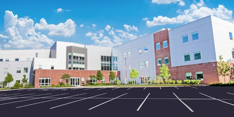  Contemporary rehab center featuring a blend of brick and white exterior, expansive parking, and lush landscaping under a bright sky.