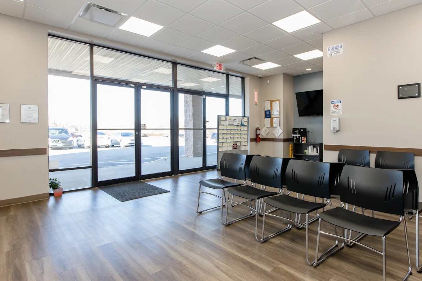 Bright waiting room near the facility entrance with black chairs, television, and wood-look flooring