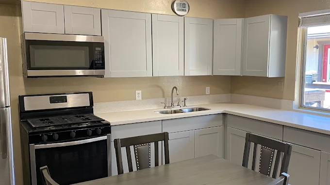 Simple kitchen with white cabinets, stainless steel stove & microwave, small dining table.