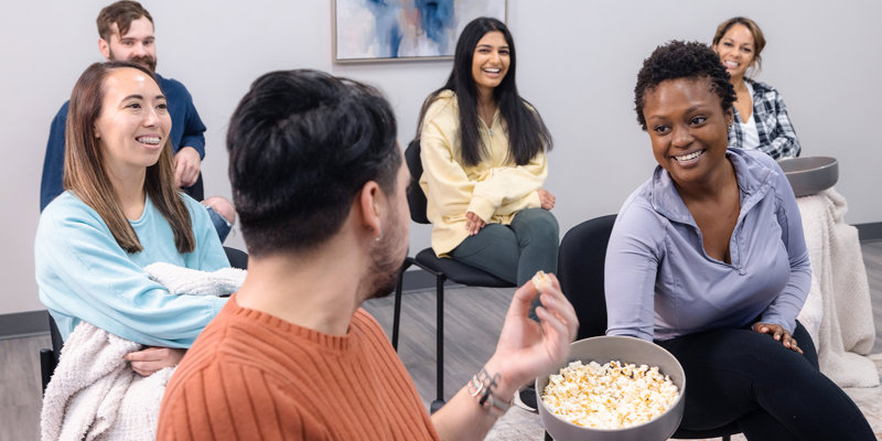  A joyful group of people sitting together, sharing popcorn and laughing, creating a warm and friendly atmosphere in a casual setting.