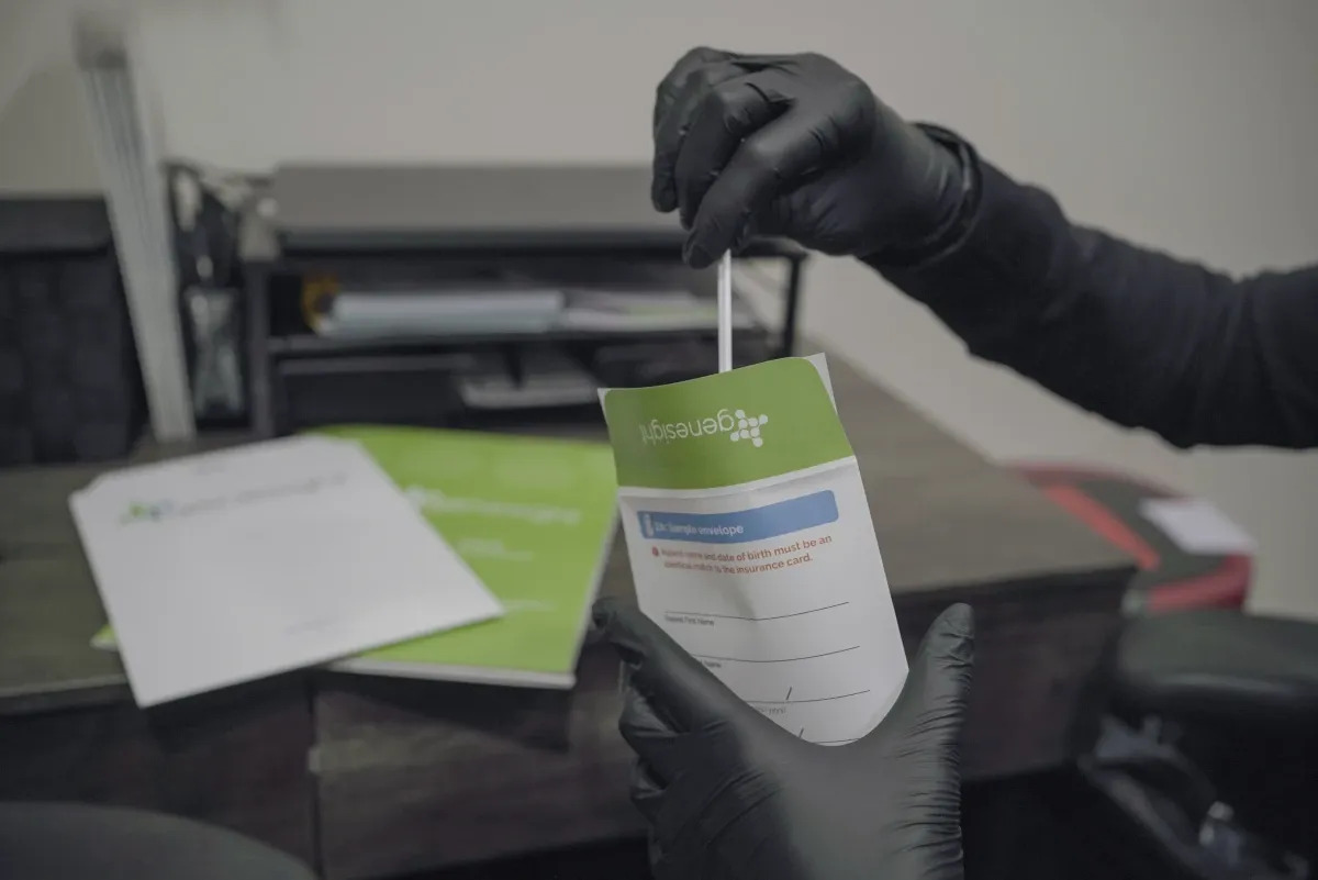 Gloved hand holding a genetic testing swab kit.