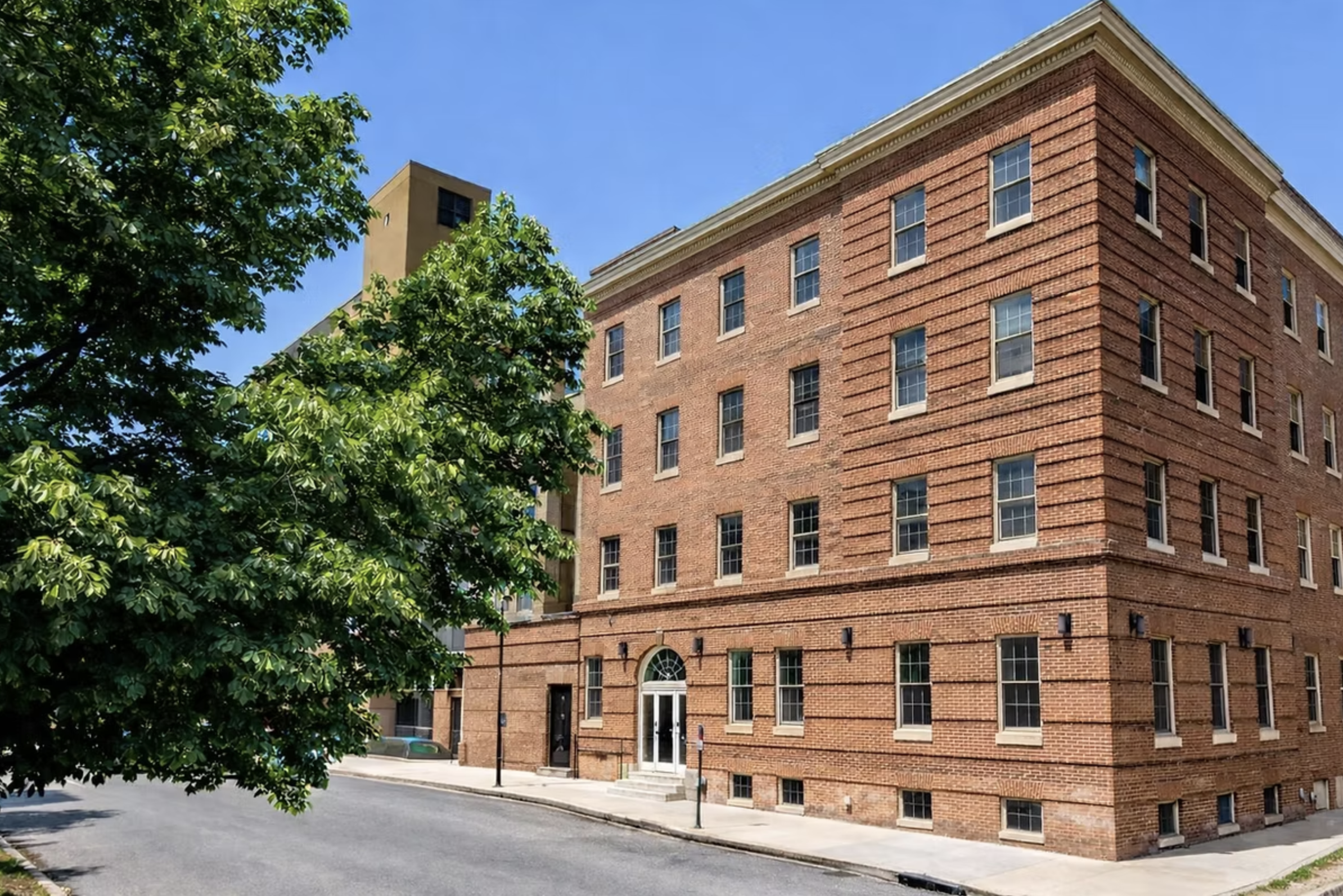 Multi-story red brick facility building along a tree-lined street