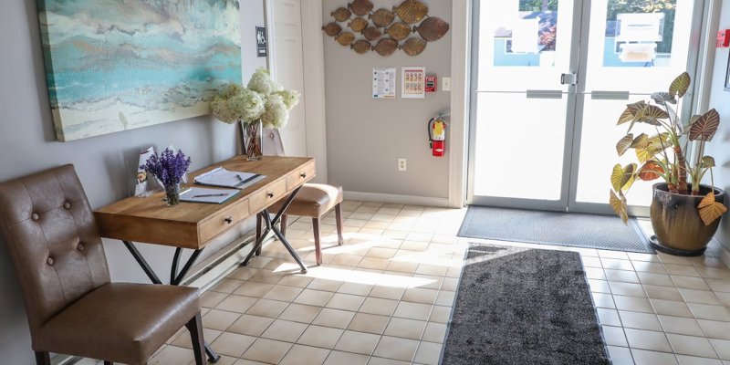 A bright, welcoming entrance with a wooden desk, leather chairs, and vibrant decor, featuring large windows that let in plenty of natural light.