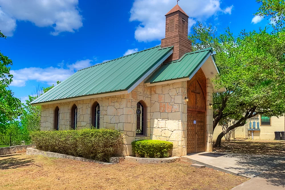 Small stone chapel with green roof and arched windows