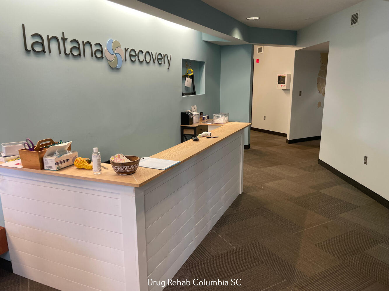 Reception area with a light wood desk and a "Lantana Recovery" sign