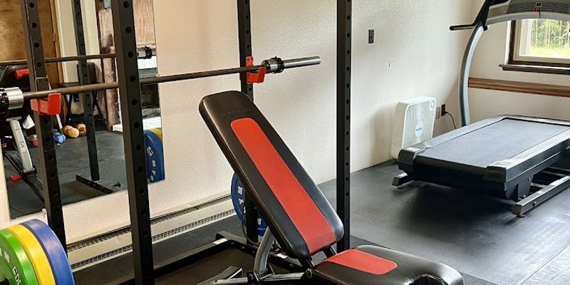 A well-equipped fitness room featuring a power rack, adjustable bench, treadmill, and weights, offering a versatile workout space.