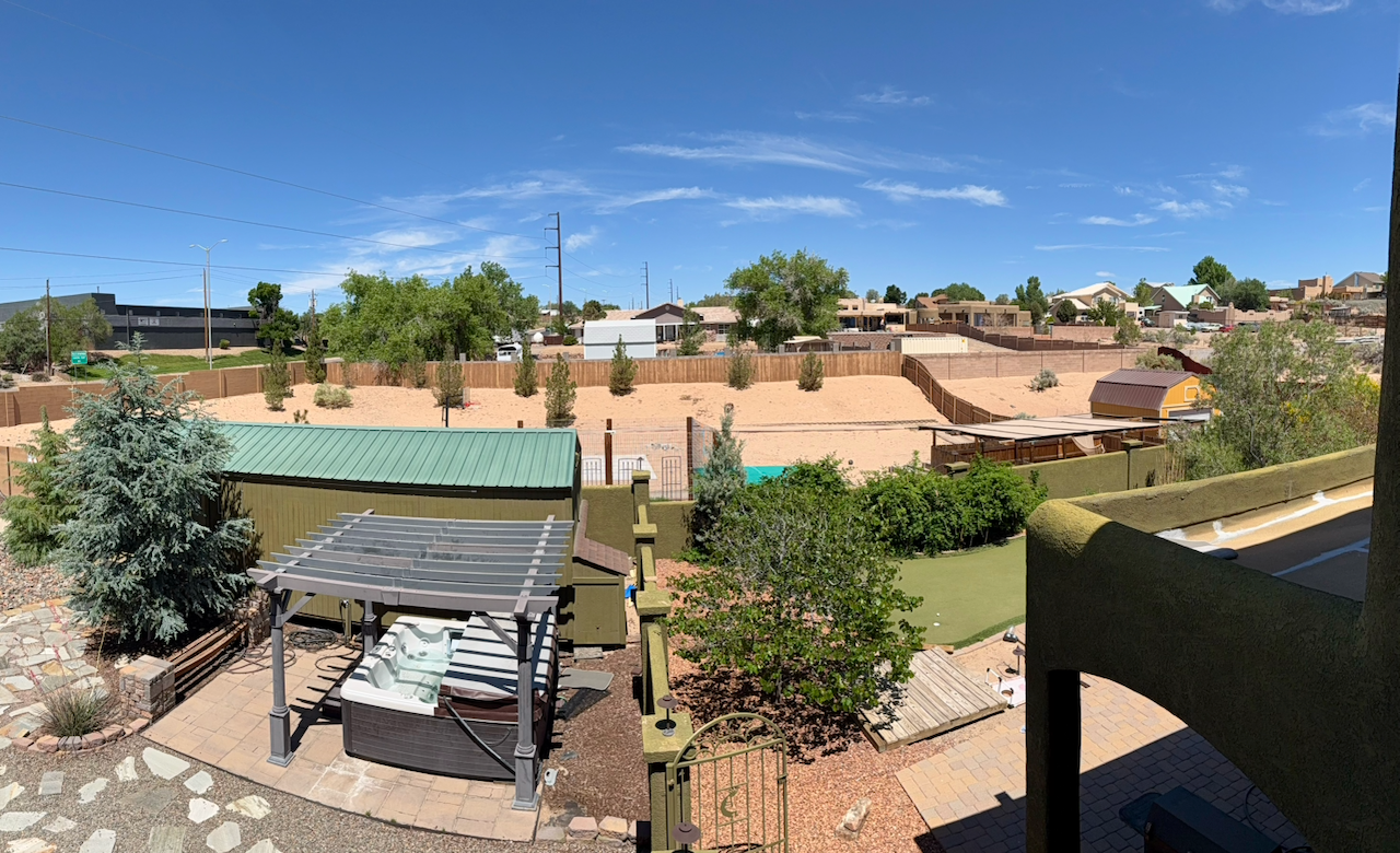 Elevated view of landscaped outdoor grounds with a covered hot tub, pathways, trees, and fenced recreation space
