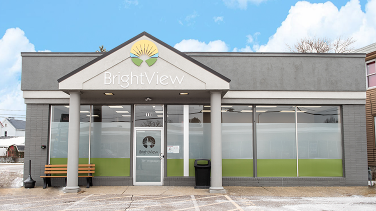 Exterior of BrightView Health Dover with gray facade, BrightView logo above the entrance, large front windows, bench, and accessible parking area